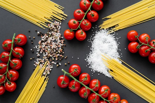 Poser à plat avec des pâtes crues près de tomates cerises et du sel sur fond noir — Photo de stock