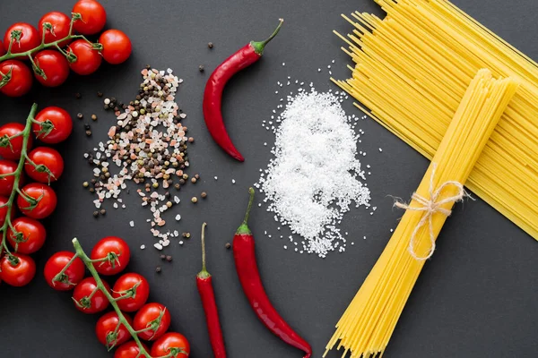 Вид сверху на экологически чистые овощи рядом с сырыми спагетти и солью на черном фоне — стоковое фото