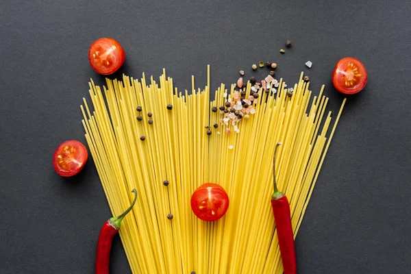 Flat lay of spices and chili peppers on raw spaghetti on black background — Stock Photo