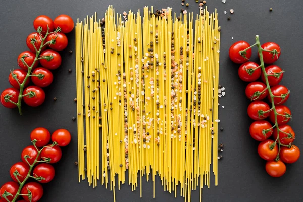 Top view of cherry tomatoes near raw spaghetti and spices on black background — Stock Photo