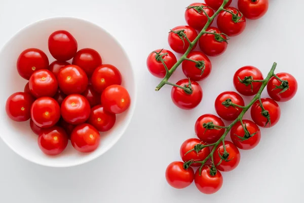 Vista superior de tomates cherry rojos maduros en ramas y en tazón sobre fondo blanco - foto de stock