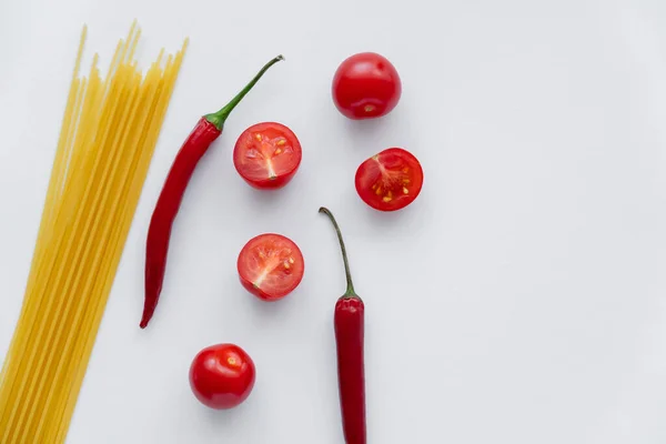 Vista superior de pimentas e tomates cereja perto de macarrão cru no fundo branco — Fotografia de Stock