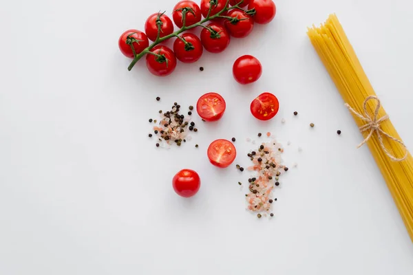 Top view of raw cherry tomatoes near spices and macaroni on white background — Stock Photo