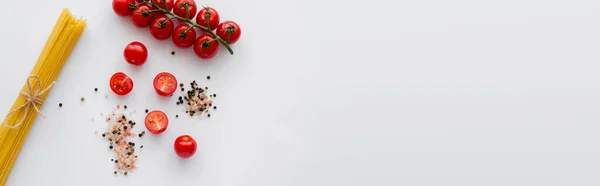 Vista dall'alto della pasta cruda vicino tagliata pomodorini e spezie su sfondo bianco, banner — Foto stock