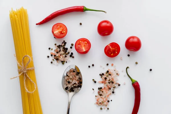 Top view of raw pasta near spices with cherry tomatoes and chili pepper on white background — Stock Photo