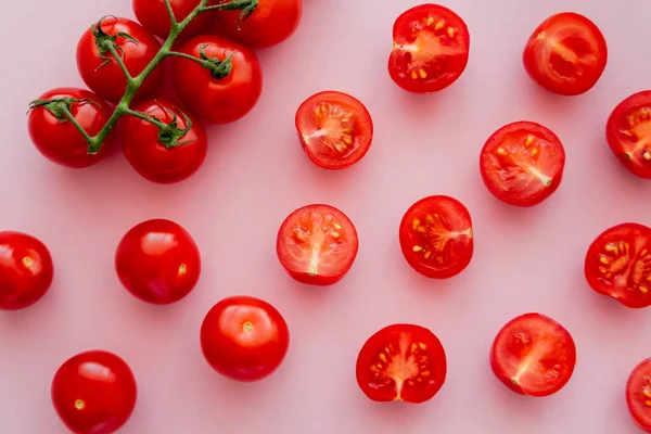 Vue du dessus des tomates cerises coupées et entières sur branche sur fond rose — Photo de stock