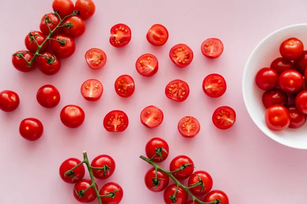 Vue du dessus des tomates cerises mûres dans un bol et sur les branches sur fond rose — Photo de stock