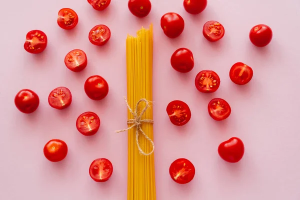 Puesta plana de pasta sin cocer y tomates cherry en la superficie rosa - foto de stock