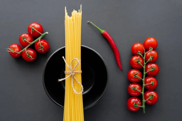 Vista dall'alto degli spaghetti crudi sulla ciotola vicino alle verdure fresche sulla superficie nera — Foto stock