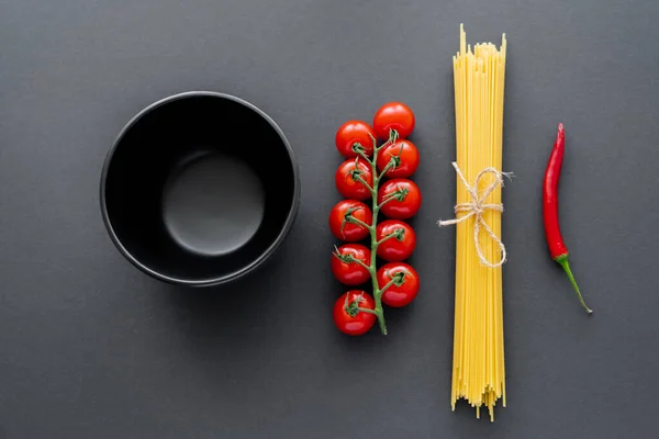 Vue du dessus du bol près des légumes frais et des pâtes non cuites sur la surface noire — Photo de stock