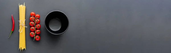 Vista superior de macarrão não cozido perto da tigela e legumes frescos na superfície preta, banner — Fotografia de Stock