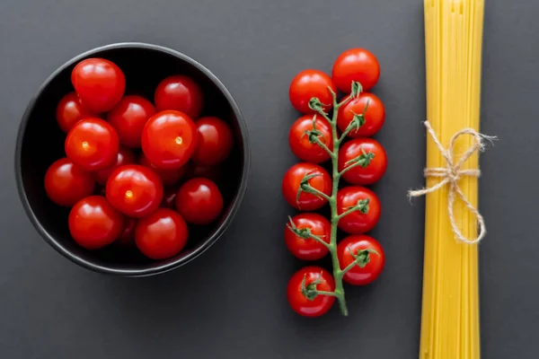 Draufsicht auf Kirschtomaten in Schüssel in der Nähe ungekochter Spaghetti auf schwarzer Oberfläche — Stockfoto