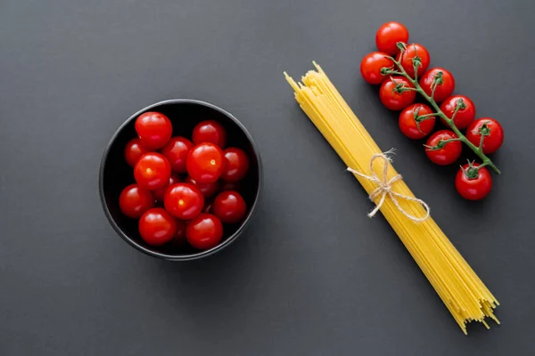 Vista superior de tomates cereja e massas não cozidas na superfície preta — Fotografia de Stock