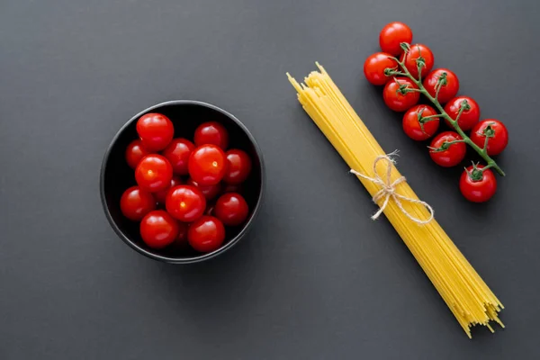 Top view of cherry tomatoes and uncooked pasta on black surface — Stock Photo