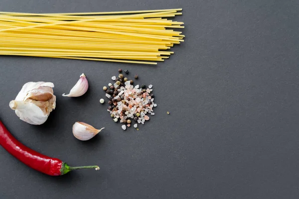 Top view of vegetables and spices near uncooked spaghetti on black surface — Stock Photo
