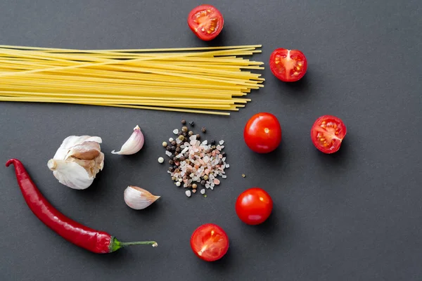 Draufsicht auf rohe Pasta in der Nähe von Gewürzen und Bio-Gemüse auf schwarzer Oberfläche — Stockfoto