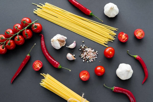 Draufsicht auf frisches Gemüse mit Knoblauch in der Nähe ungekochter Pasta und Gewürzen auf schwarzer Oberfläche — Stockfoto