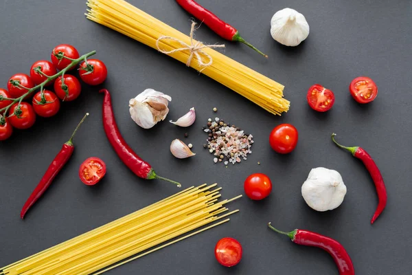 Top view of uncooked pasta near fresh vegetables and spices on black surface — Stock Photo