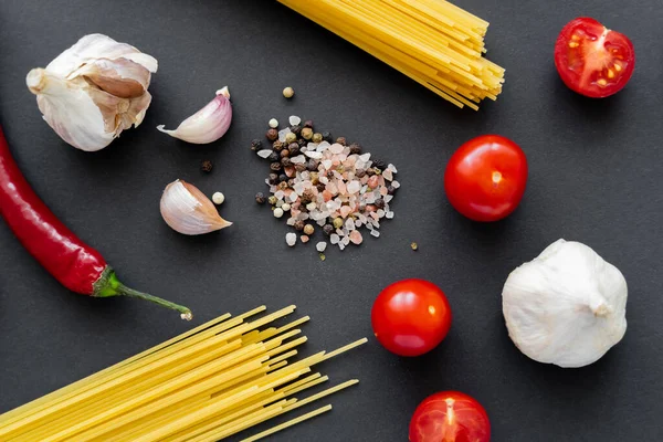 Vista superior de especiarias perto de macarrão cru e legumes na superfície preta — Fotografia de Stock