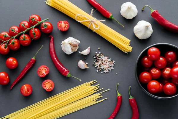 Vue de dessus des légumes naturels près des épices et des pâtes non cuites sur la surface noire — Photo de stock