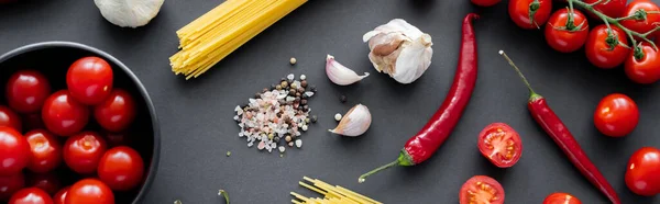 Top view of fresh vegetables near spices with garlic and raw pasta on black surface, banner — Stock Photo