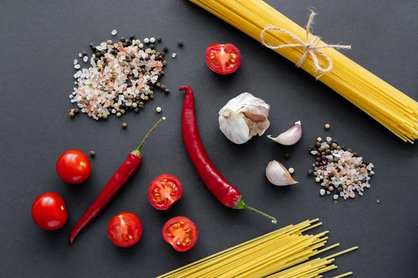 Vue de dessus des spaghettis non cuits près des épices aromatiques et des légumes sur la surface noire — Photo de stock