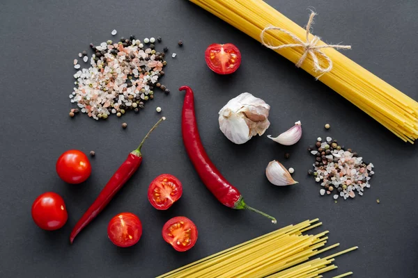 Top view of uncooked spaghetti near aromatic spices and vegetables on black surface — Stock Photo