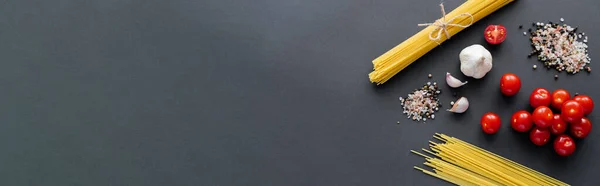 Top view of raw spaghetti near garlic and spices on black surface with copy space, banner — Stock Photo