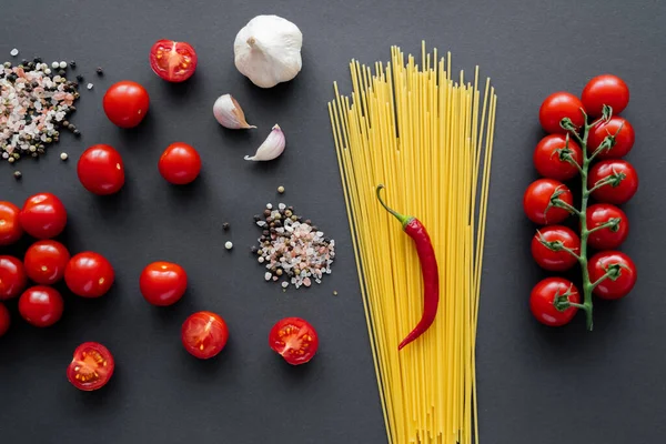 Vue de dessus des légumes naturels et des épices près des pâtes non cuites sur la surface noire — Photo de stock