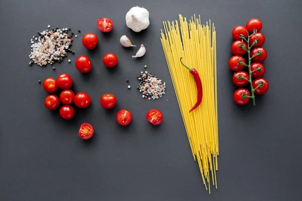 Vista superior de vegetais frescos perto de especiarias aromáticas e massas cruas na superfície preta — Fotografia de Stock