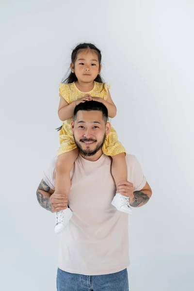 Happy asian child sitting on shoulders of tattooed father isolated on grey — Stock Photo