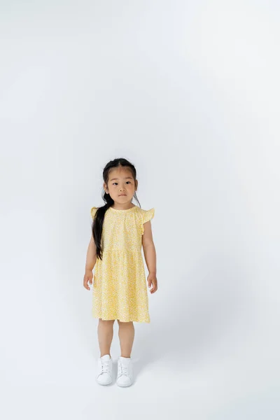 Полная длина азиатской дошкольницы в желтом платье, стоящей на сером — стоковое фото