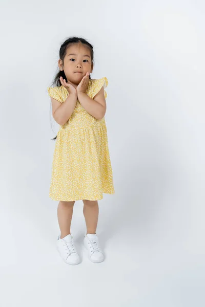 Повна довжина азіатської дівчини дошкільника в жовтій сукні позує, стоячи на сірому — стокове фото