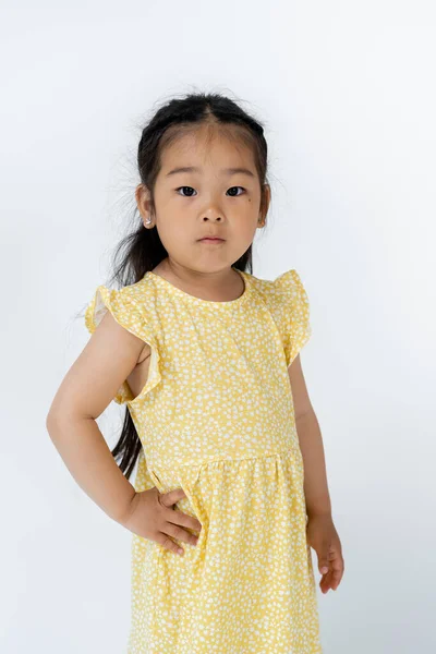 Брюнетка дошкольница азиатская девушка позирует с рукой на бедре, глядя на камеру, изолированную на сером — стоковое фото