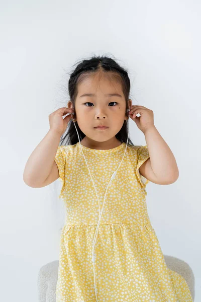 Morena pré-escolar asiático menina vestindo fones de ouvido com fio enquanto olha para a câmera isolada no cinza — Fotografia de Stock