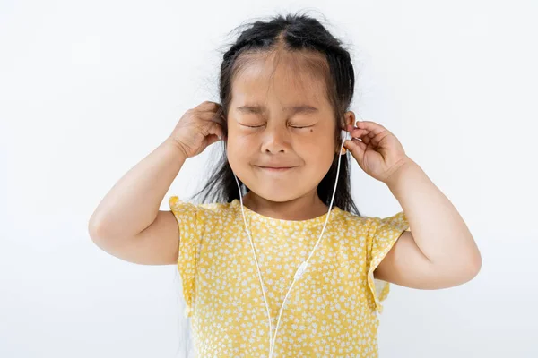 Pleased asian girl with closed eyes wearing wired earphones isolated on grey — Stock Photo