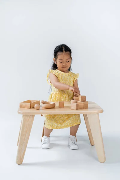 Pleine longueur de asiatique enfant jouer avec en bois jouets sur table sur gris — Photo de stock