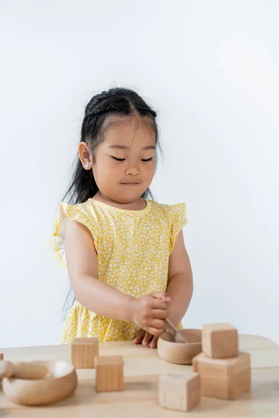 Brunette asian girl holding wooden spoon near bowl while playing isolated on grey — Stock Photo