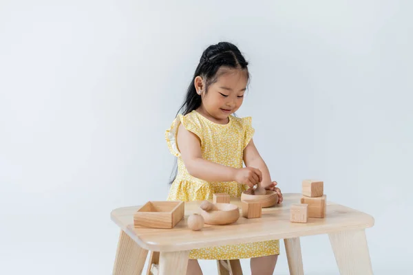 Feliz asiático menina segurando madeira colher perto tigela enquanto joga isolado no cinza — Fotografia de Stock