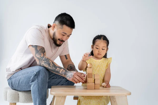 Lächelnder asiatischer Vater spielt Holzwürfel mit Vorschultochter isoliert auf grau — Stockfoto