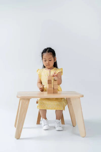 Asian preschooler girl in yellow dress playing with wooden shapes on grey — Stock Photo