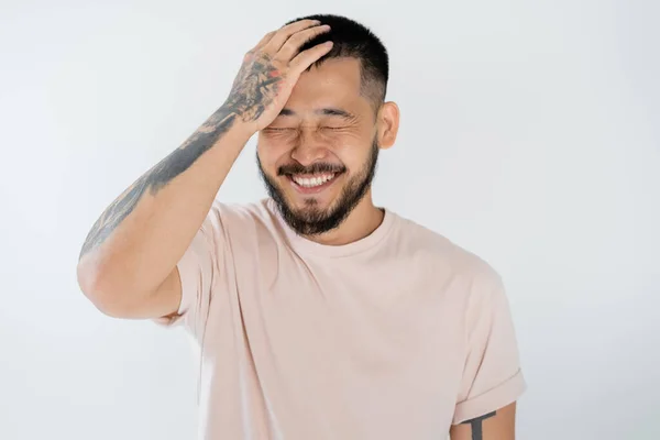 Retrato de hombre asiático feliz con barba y ojos cerrados sonriendo aislado en gris - foto de stock