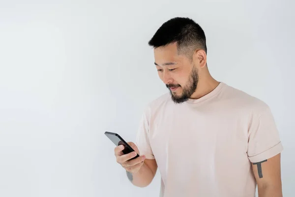 Bärtiger asiatischer Mann mit Tätowierungen mit Smartphone isoliert auf grau — Stockfoto