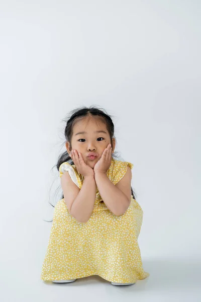 Asiatico bambino in giallo abito bronzante labbra e seduta su grigio — Foto stock