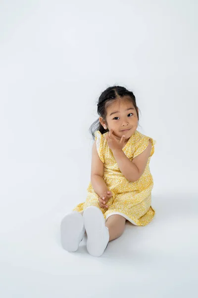 Full length of cute asian child in yellow dress sitting on grey — Stock Photo