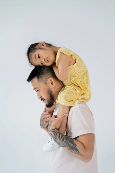 Ásia pai com barba segurando pré-escolar filha no ombros isolado no cinza — Fotografia de Stock