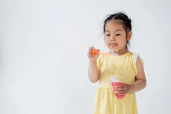 Pré-escolar asiático menina no amarelo vestido segurando garrafa com sabão bolhas isolado no cinza — Fotografia de Stock