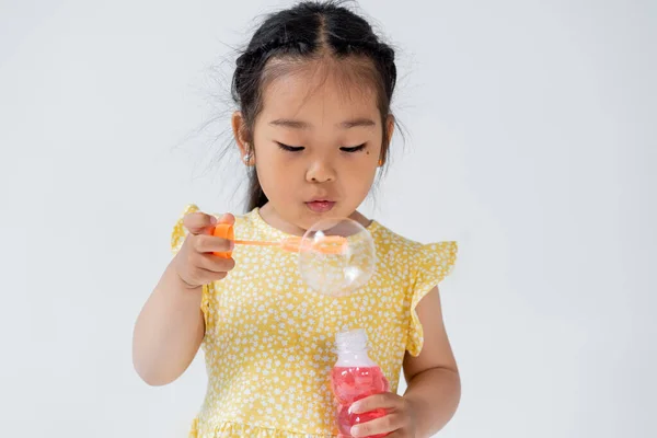 Preschooler asian girl in dress holding bottle with soap bubbles isolated on grey — Stock Photo