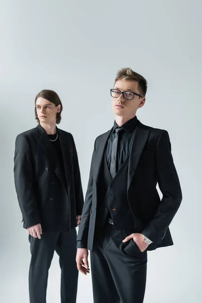 Elegant gay in eyeglasses looking at camera near boyfriend isolated on grey — Stock Photo