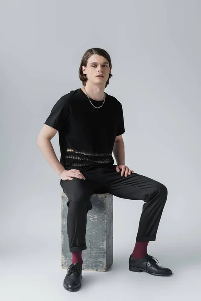 Stylish man sitting on concrete block on grey background — Stock Photo